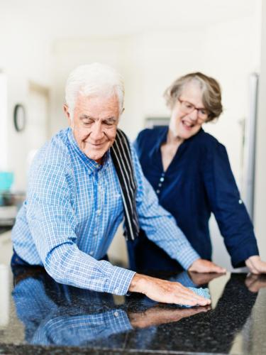 Senior man cleans the kitchen as contented woman watches him