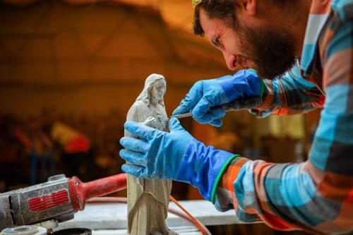 Focused Caucasian male sculptor, using hand tools to carve small details on a sculpture